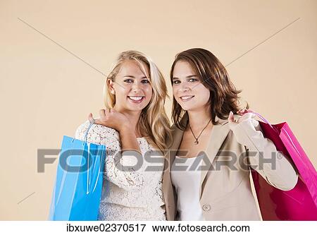 Two young women carrying shopping bags while shopping together View Large Photo Image Stock Photo - Two young women carrying shopping bags while shopping together. Fotosearch