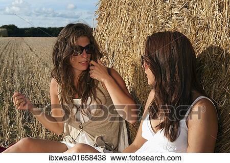 "Two young women sitting on a harvested grain field in front of a bale of straw and talking, Finistere departement, Brittany region, France, Europe" View Large Photo Image Stock Photo - "Two young women sitting on a harvested grain field in front of a bale of straw and talking, Finistere departement, Brittany region, France, Europe". Fotosearch