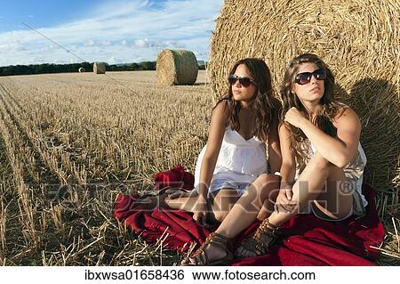 "Two young women sitting on a harvested grain field in front of a bale of straw and talking, Finistere departement, Brittany region, France, Europe" View Large Photo Image Stock Photograph - "Two young women sitting on a harvested grain field in front of a bale of straw and talking, Finistere departement, Brittany region, France, Europe". Fotosearch