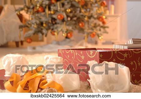 Picture - Unwrapped present in front of a Christmas tree. Fotosearch