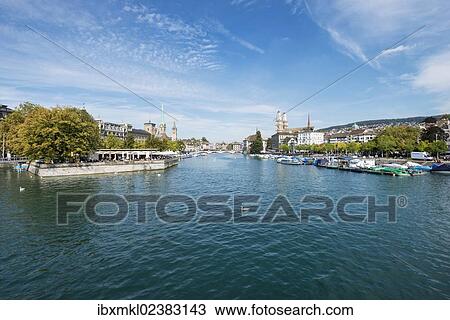 Stock Image - "View from Quaibruecke bridge over the Limmat river, beer garden on the island auf Bauschaenzli, left, and the marina with the old town promenade and the twin towers of the Grossmuenster church, right, Zurich, Canton of Zurich, Switzerland, Europe". Fotosearch