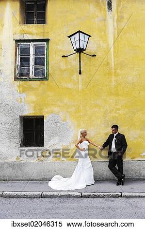 Stock Photography - "Wedding, bride and groom holding hands in front of an old, yellow wall". Fotosearch