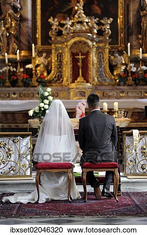 Stock Image - "Wedding in church, bride and groom sitting in front of the altar". Fotosearch