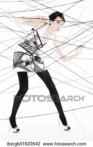 Stock Image - "Woman, 24, dressed in the style of the 60s, standing between spanned threads, symbolic image network". Fotosearch