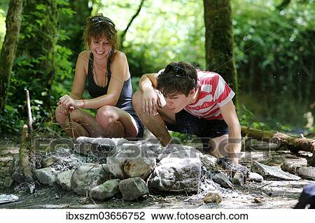 Stock Image - Woman and man having a barbecue in a clearing. Fotosearch