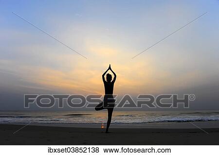 Stock Photo - "Woman doing yoga on a beach at dusk, Kerala, India, Asia". Fotosearch