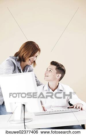 Woman helping a boy on a computer View Large Photo Image Stock Photograph - Woman helping a boy on a computer. Fotosearch