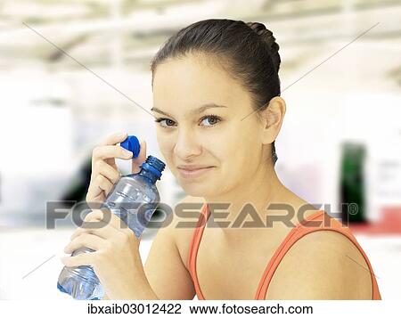 Stock Image - Woman holding a water bottle in a fitness studio. Fotosearch