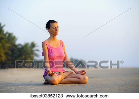 Stock Image - "Woman meditating on a beach in the evening, Kerala, India, Asia". Fotosearch