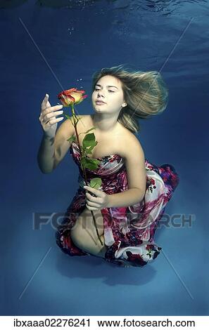 Stock Image - Woman presenting underwater fashion in pool. Fotosearch