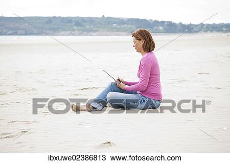 Woman sitting with a digital tablet on a beach View Large Photo Image Stock Image - Woman sitting with a digital tablet on a beach. Fotosearch