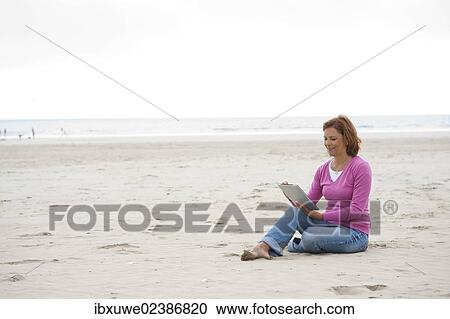 Woman sitting with a digital tablet on a beach View Large Photo Image Stock Image - Woman sitting with a digital tablet on a beach. Fotosearch