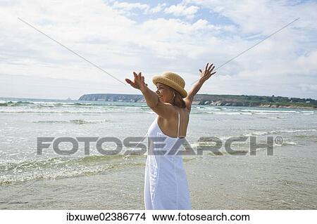 Woman standing with her arms outstretched on a beach View Large Photo Image Picture - Woman standing with her arms outstretched on a beach. Fotosearch
