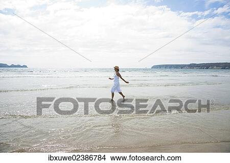 Picture - Woman standing with her arms outstretched on a beach. Fotosearch