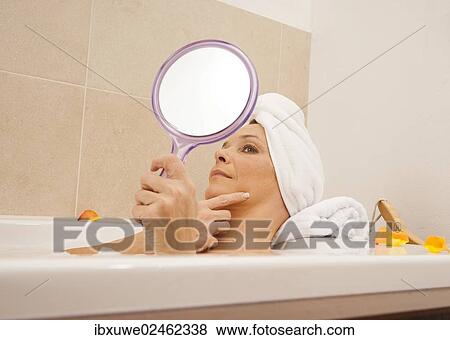 Woman taking a bath and looking at her face with a mirror View Large Photo Image Stock Photo - Woman taking a bath and looking at her face with a mirror. Fotosearch