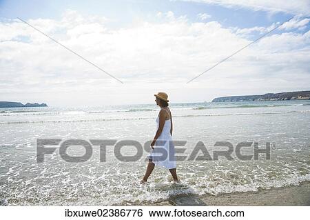 Woman walking through small waves on a beach View Large Photo Image Stock Photograph - Woman walking through small waves on a beach. Fotosearch