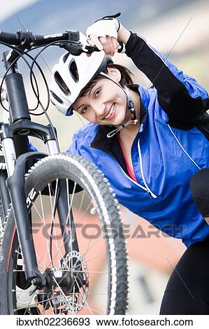 Stock Image - "Woman wearing a cycling helmet, with her bike". Fotosearch