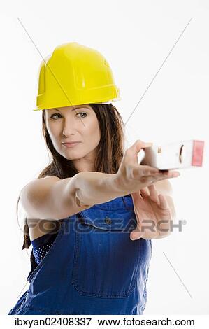 Woman wearing blue overalls and a hardhat holding a spirit level View Large Photo Image Stock Photo - Woman wearing blue overalls and a hardhat holding a spirit level. Fotosearch