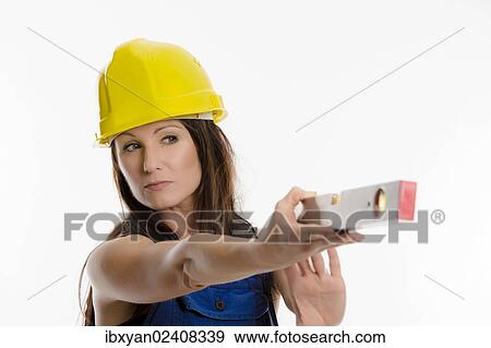 Woman wearing blue overalls and a hardhat holding a spirit level View Large Photo Image Stock Photo - Woman wearing blue overalls and a hardhat holding a spirit level. Fotosearch
