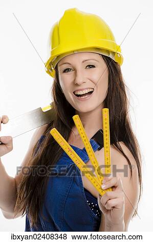 Woman wearing blue overalls and a hardhat holding a folding carpenter's ruler and a spirit level View Large Photo Image Stock Photo - Woman wearing blue overalls and a hardhat holding a folding carpenter's ruler and a spirit level. Fotosearch