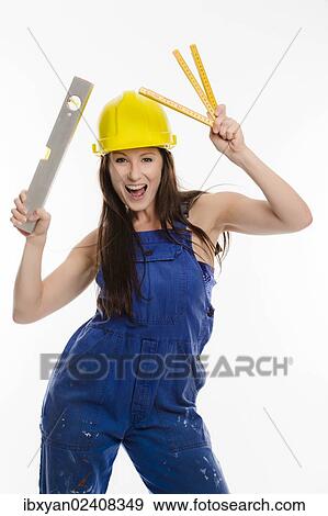 Woman wearing blue overalls and a hardhat holding a folding carpenter's ruler and a spirit level View Large Photo Image Stock Photo - Woman wearing blue overalls and a hardhat holding a folding carpenter's ruler and a spirit level. Fotosearch