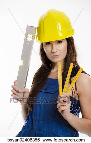 Woman wearing blue overalls and a hardhat holding a folding carpenter's ruler and a spirit level View Large Photo Image Stock Photograph - Woman wearing blue overalls and a hardhat holding a folding carpenter's ruler and a spirit level. Fotosearch