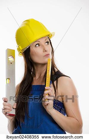 Stock Photography - Woman wearing blue overalls and a hardhat holding a folding carpenter's ruler and a spirit level. Fotosearch