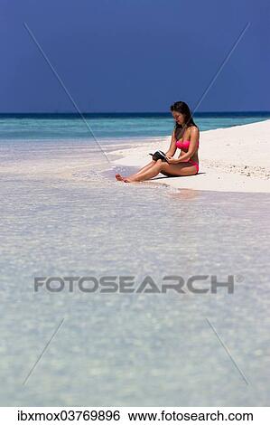 Stock Photograph - "Woman with a book sitting on the beach, Male, North Male Atoll, Maldives, Asia". Fotosearch