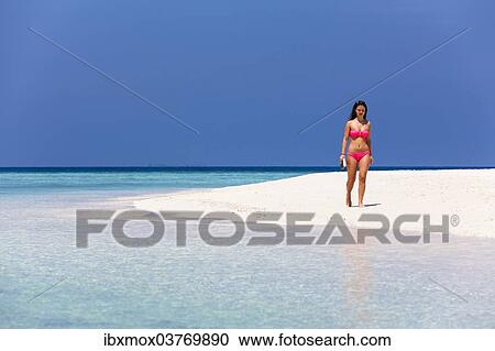 Stock Image - "Woman with a book walking along the beach, Male, North Male Atoll, Maldives, Asia". Fotosearch