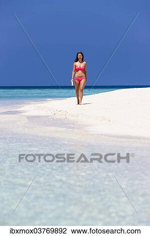 Stock Image - "Woman with a book walking along the beach, Male, North Male Atoll, Maldives, Asia". Fotosearch