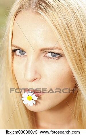 Stock Image - "Woman with a daisy in her mouth, Thuringer Becken, Thuringer Wald, Thuringia, Germany, Europe". Fotosearch