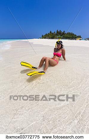 Stock Photography - "Woman with flippers and diving goggles sitting on a sand bank, Indian Ocean, Maldives, Asia". Fotosearch