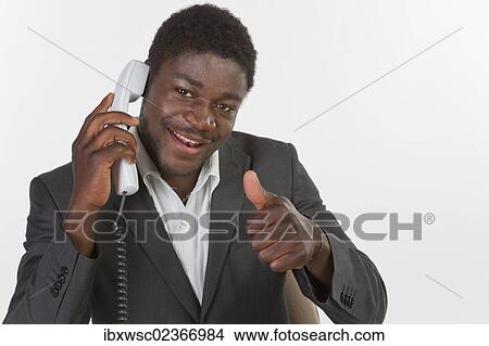 "Young black man in a suit making a phone call in an office, smiling with thumbs up gesture" View Large Photo Image Picture - "Young black man in a suit making a phone call in an office, smiling with thumbs up gesture". Fotosearch