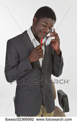 Stock Image - "Young black man in a suit making a phone call in an office, looking pensively". Fotosearch