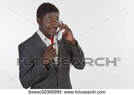 "Young black man in a suit making a phone call in an office, looking pensively" View Large Photo Image Stock Photography - "Young black man in a suit making a phone call in an office, looking pensively". Fotosearch