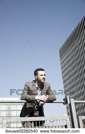 Stock Image - Young business man standing pensively against a railing. Fotosearch