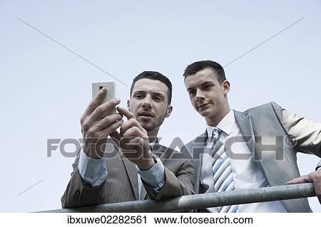 Stock Image - Young businessman checking his mobile phone and showing something to a colleague. Fotosearch