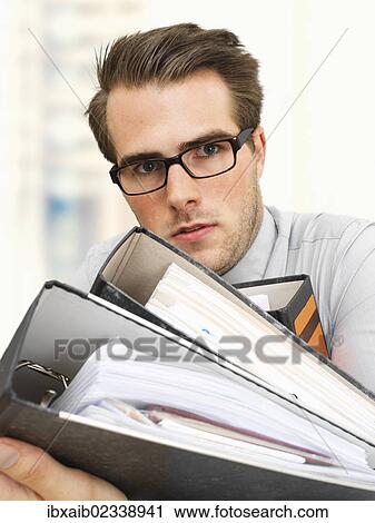 "Young businessman wearing glasses carrying document files, serious face, overworked" View Large Photo Image Stock Image - "Young businessman wearing glasses carrying document files, serious face, overworked". Fotosearch