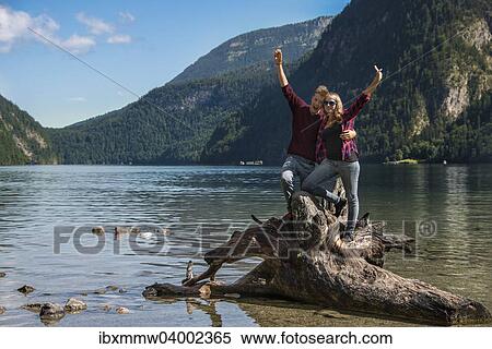 "Young couple on a fallen tree trunk stretching their arms up in the air, Konigssee, National Park Berchtesgaden, Berchtesgadener Land district, Upper Bavaria, Bavaria, Germany, Europe" View Large Photo Image Stock Photography - "Young couple on a fallen tree trunk stretching their arms up in the air, Konigssee, National Park Berchtesgaden, Berchtesgadener Land district, Upper Bavaria, Bavaria, Germany, Europe". Fotosearch