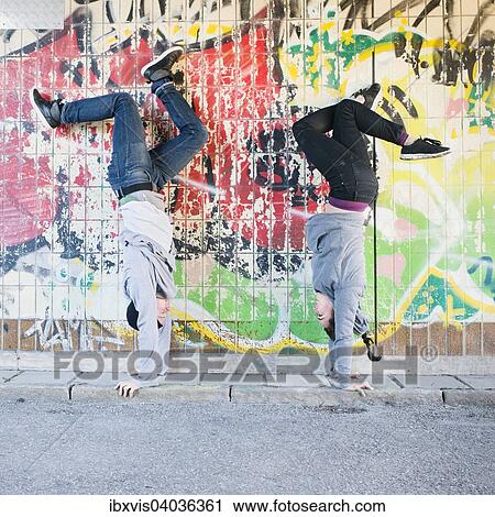 Stock Image - "Young man and woman doing handstand in front of grafitti wall in urban area, Sweden, Europe". Fotosearch