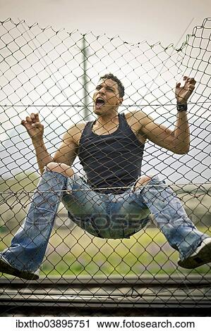 Stock Image - Young man climbing a fence. Fotosearch