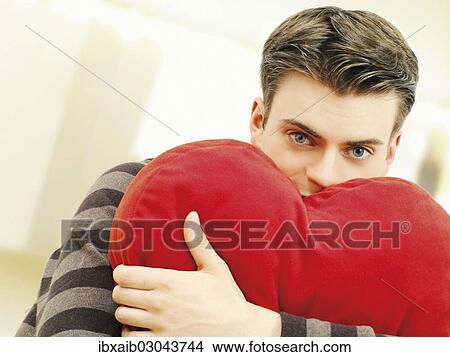 Young man holding a heart-shaped pillow View Large Photo Image Picture - Young man holding a heart-shaped pillow. Fotosearch