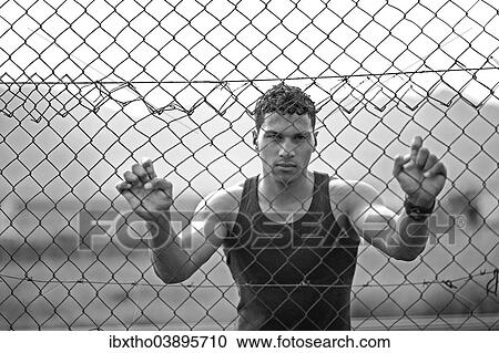 Stock Image - Young man holding onto a fence. Fotosearch