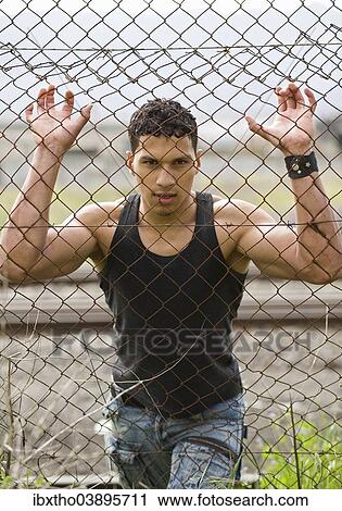 Young man holding onto a fence View Large Photo Image Stock Image - Young man holding onto a fence. Fotosearch