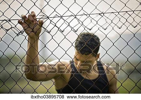 Stock Photo - Young man holding onto a fence. Fotosearch