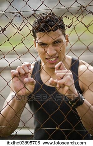 Young man holding onto a fence View Large Photo Image Stock Photograph - Young man holding onto a fence. Fotosearch