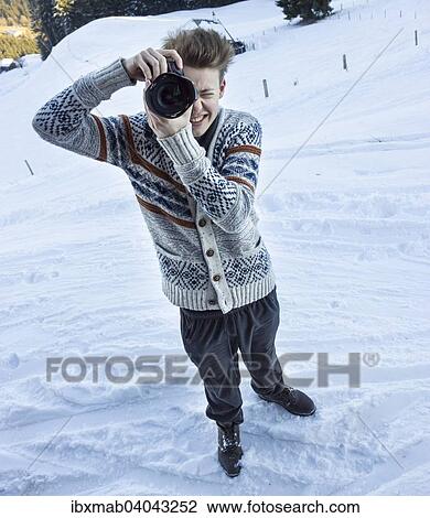 Stock Image - "Young man in the snow taking a picture with a digital SLR camera, Hochbrixen, Brixen im Thale, Tyrol, Austria, Europe". Fotosearch