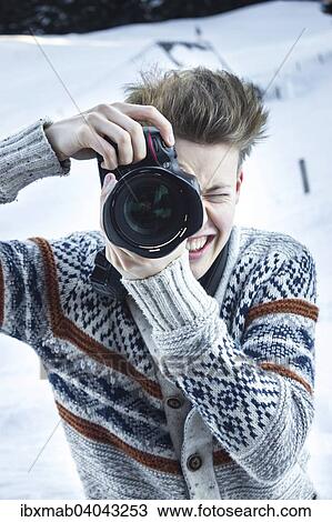 Stock Image - "Young man in the snow taking a picture with a digital SLR camera, Hochbrixen, Brixen im Thale, Tyrol, Austria, Europe". Fotosearch