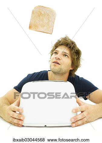 Young man looking at a slice of toast as it pops out of a toaster View Large Photo Image Stock Photo - Young man looking at a slice of toast as it pops out of a toaster. Fotosearch