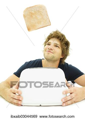 Young man looking at a slice of toast as it pops out of a toaster View Large Photo Image Stock Photo - Young man looking at a slice of toast as it pops out of a toaster. Fotosearch